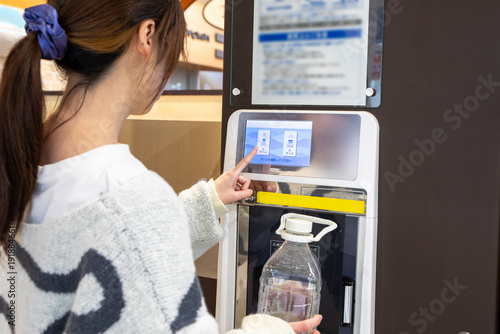 スーパーのウォーターサーバーで水を汲む女性