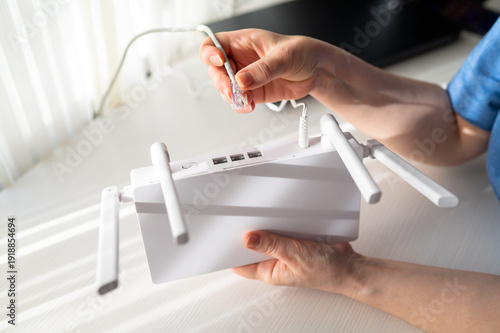 Close-up of Woman Hands Plugging Ethernet RJ45 Cable into White WiFi Router on Desk