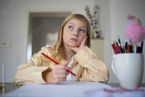 Pensive Young Girl Looking Up While Holding a Pencil and Drawing