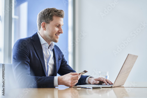 Businessman holding credit card and using laptop at desk in office