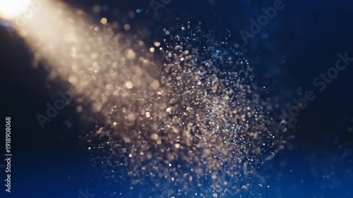 Bright spotlight illuminates sparkling dust particles against a dark blue