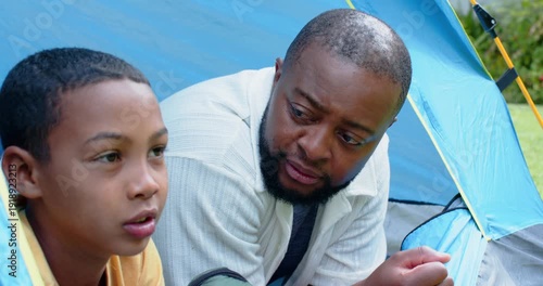 African American father and son at tent opening, father leaning, speaking, reassuring son smiling