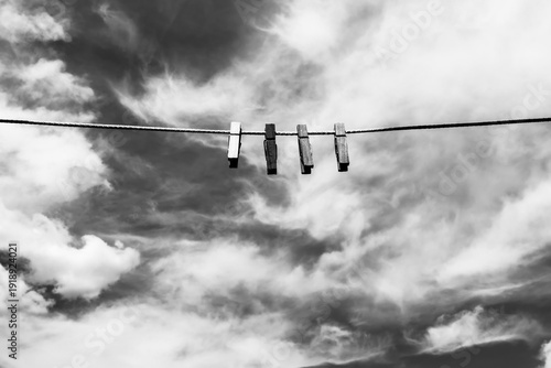 Wooden clothespins hanging on a clothesline on a cloudscape background, black white photo