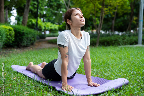 Beautiful young woman practicing Padmasana on yoga mat outdoors, space for text.