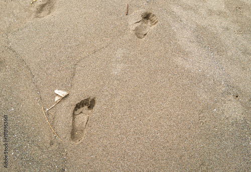 Foto Detailed human footprints are impressed into the golden beach sand showing natural textures, shadows and step patterns in the warm sunlight