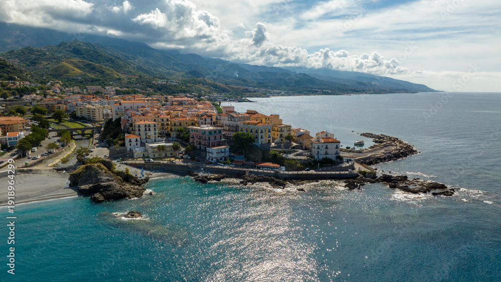 Fototapeta premium Aerial view of a historic coastal village in Italy, with traditional multi-story buildings and terracotta roofs clustered on a rocky cliff overlooking the blue sea. It is Diamante, in Calabria.
