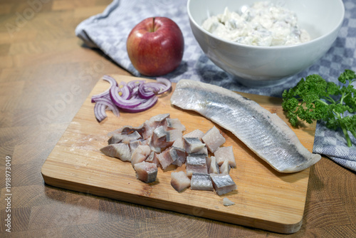 Chopped soused herring fillets on a cutting board, onions, apple, and herbs to make a fresh herring salad, ingredients for a traditional fish dish, copy space, selected focus