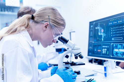 Closeup woman scientist looking in microscope while working on medical research in science laboratory with biology data on computer screen