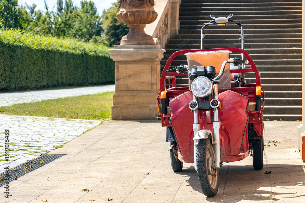 Fototapeta premium A motorized tricycle of gardener is parked under a stairway