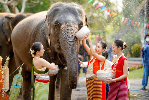 Closeup group of beautiful Thai young lady in the Thai traditional dress play to sprinkle and splash water from silver bow with Asia elephant on the Thai New Year's Day or Songkran water festival