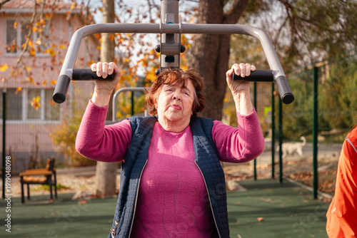 Fotografie Elderly Caucasian woman trains on street gym machines during post surgery recovery