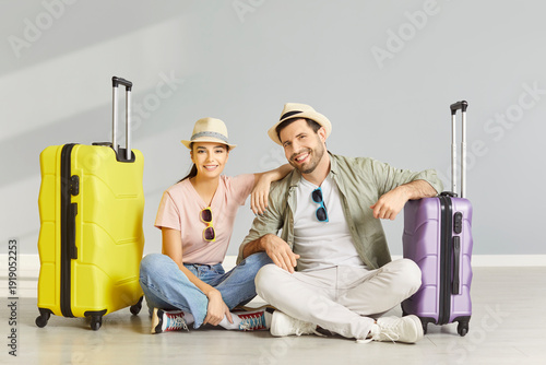 Fototapeta Smiling young couple sitting on floor between suitcases in empty room, going on summer trip together