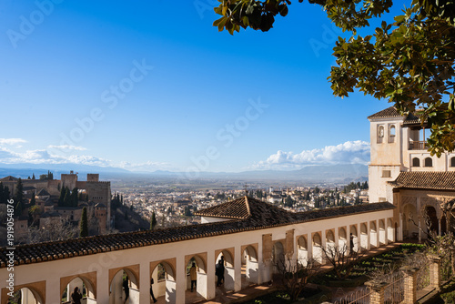 Fototapeta A breathtaking panoramic view of Granada stretching below the majestic Alhambra complex, with snow-capped Sierra Nevada mountains in the distance, showcasing Spain's winter tourism appeal