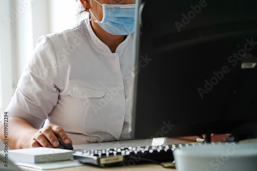 The doctor is sitting at the computer at his desk in the hospital.