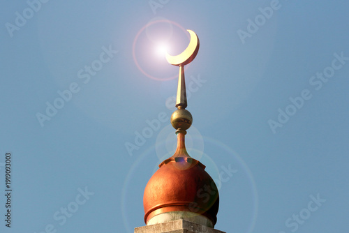 Islamic mosque dome with crescent and sun flare against deep blue sky, symbol of faith and oriental architecture.