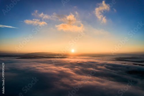 Φωτογραφία Aerial view of sun rises above blanket of clouds, casting warm golden glow over misty landscape
