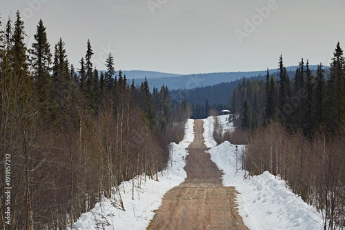A dirt road with snow on the sides in the forest