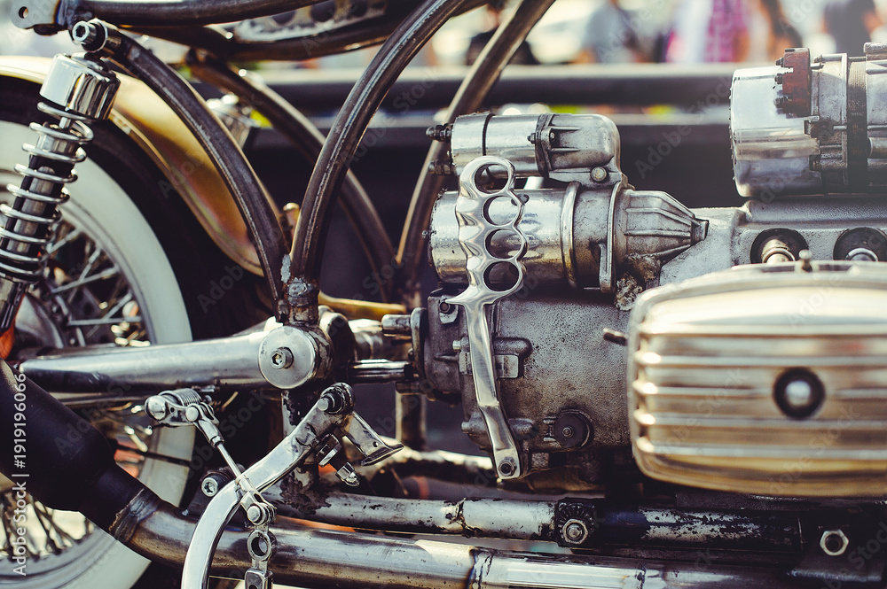Φωτογραφία A close-up horizontal shot of a motorcycle's rear section, showing a chrome shock absorber, spoked wheel with a whitewall tire, and custom metal frame
