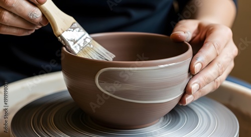 Hands shaping and painting ceramic bowl on pottery wheel with brush