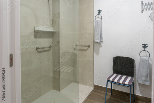 Fotografie Accessible walk-in shower featuring glass partition, grab bars, shelf, and light