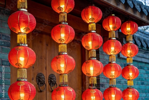 Red lanterns illuminated and hanging in rows outside a traditional wooden door with stone walls.