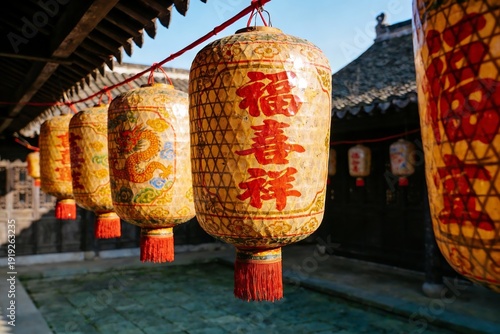 Traditional Chinese lanterns with red tassels and calligraphy hang in a courtyard, illuminated by sunlight.