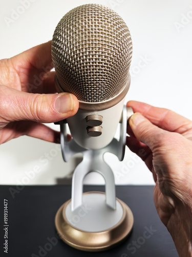Closeup isolated shot of hands holding a retro microphone on a stand, while turning a knob to raise the mic to a higher position.