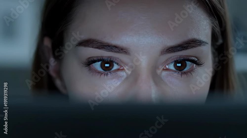 Close-up of focused young adult woman looking at laptop computer screen late at night, working.