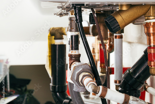 Plumbing underneath hot water heating system. Piping for a natural gas–powered heater in a closed-loop hydronic system. Plumbing service for home heating and maintaining. Selective focus.