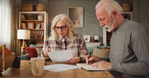 Fotografía Two seniors examine documents related to life insurance at a table in their living room