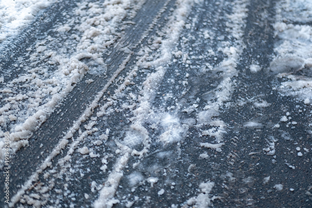 Fototapeta premium Deep tire tracks in melting snow and brown slush on urban asphalt road, pavement after heavy snowfall, wet snow melts, slippery and dangerous driving conditions in winter, messy street, transportation