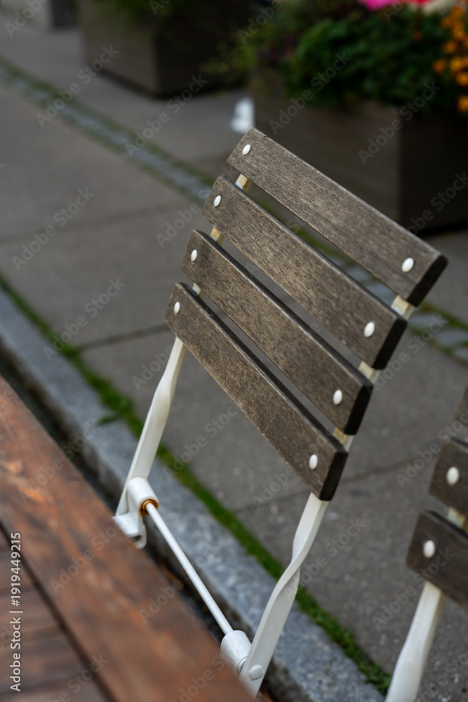 Fototapeta premium Back of a rustic outdoor chair with dark wooden slats and a white metal frame resting on a gray paved patio