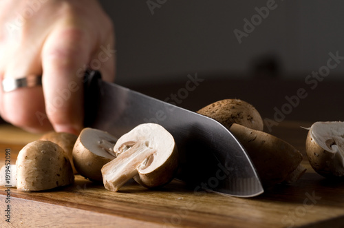 Closeup of Man Cutting Cremini Mushrooms with a Black Knife on Wood Cutting Board