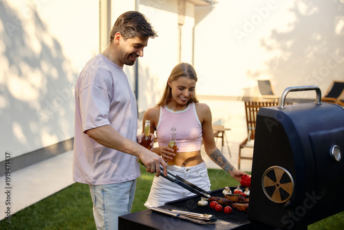 Foto Young couple grilling meat at backyard summer barbecue