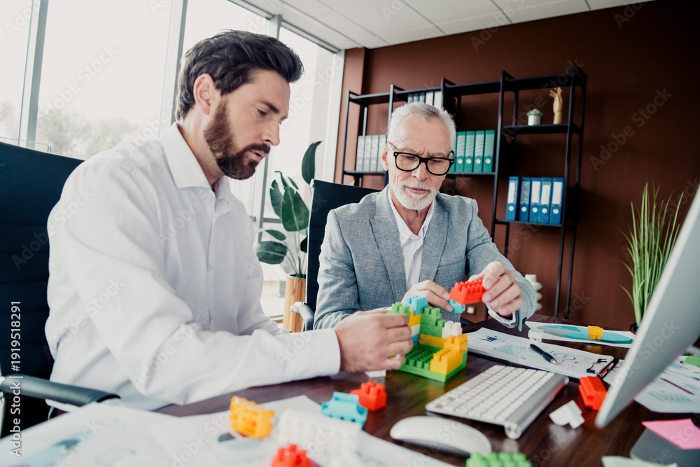 Fototapeta premium Two colleagues collaborate at a modern office desk building colorful blocks during a professional business meeting