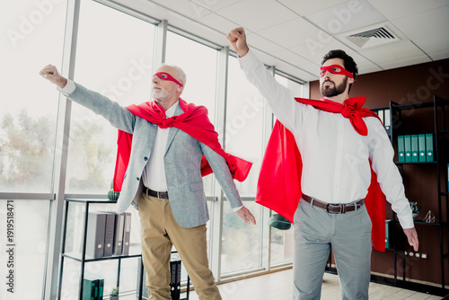 Schilderij op canvas Two businessmen in red capes strike heroic pose in modern office