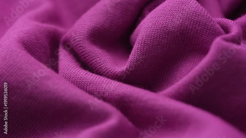 A soft dark magenta knit fabric draped in elegant, flowing folds that highlight its fine ribbed texture. Close up.