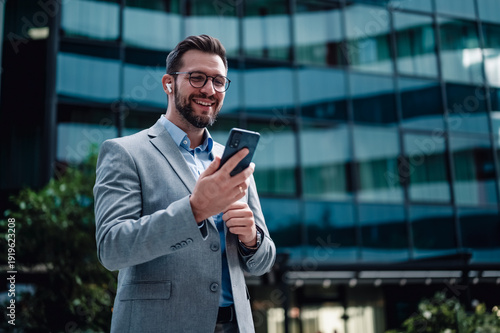 Wallpaper Mural Smiling businessman using smartphone and wireless earbuds Torontodigital.ca