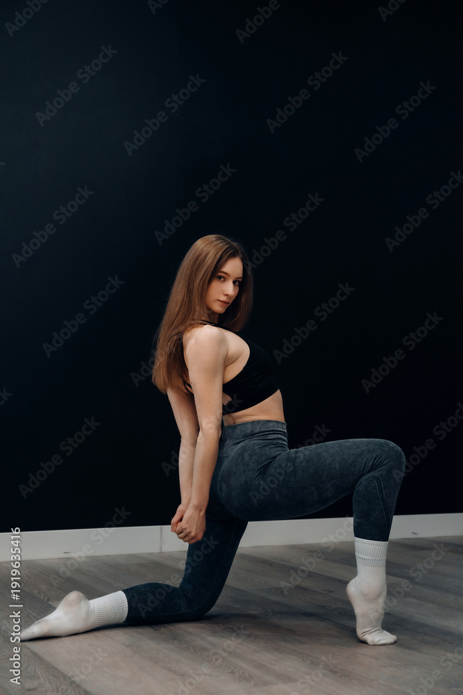 Obraz premium Beautiful young female stretches her body in activewear to keep fit and healthy during a workout session indoors
