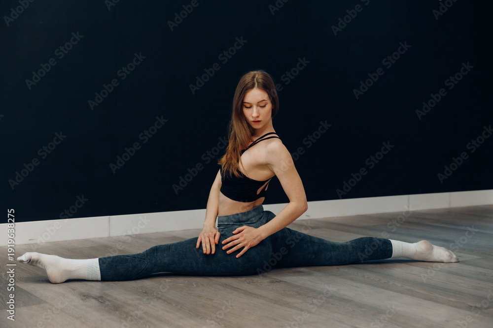 Obraz premium Beautiful young female performs seated side stretch in activewear for fitness training and healthy lifestyle in indoor gym