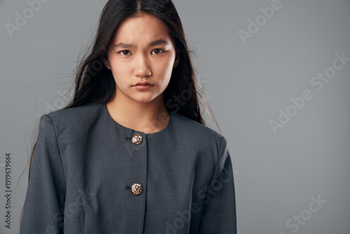 Portrait of serious young woman with long straight hair wearing dark buttoned jacket on gray background looking at camera with intense confident expression for professional style.