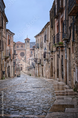 Scenic vertical view of a narrow medieval cobblestone street in Siguenza Spain leading towards the historic stone cathedral under a moody winter sky featuring traditional spanish architecture