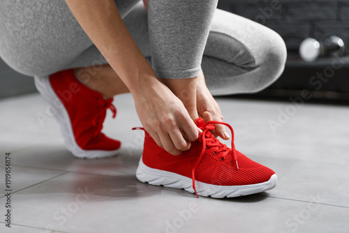 Photos Woman tying shoelace of red sneaker indoors, closeup