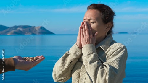 Woman refusing offered pistachios. Woman standing near seashore, repeatedly refusing offered pistachios with changing facial expressions, displaying clear signs of food rejection and aversion