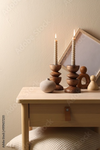 Fotografía Beautiful burning candles in candlesticks, frame and decor on wooden table near beige wall