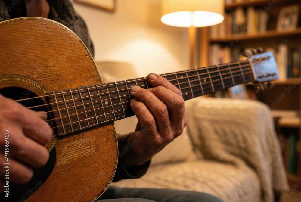 Fototapeta premium Close-up of a man's hands playing a chord on the fretboard of a wooden acoustic guitar in a cozy room.