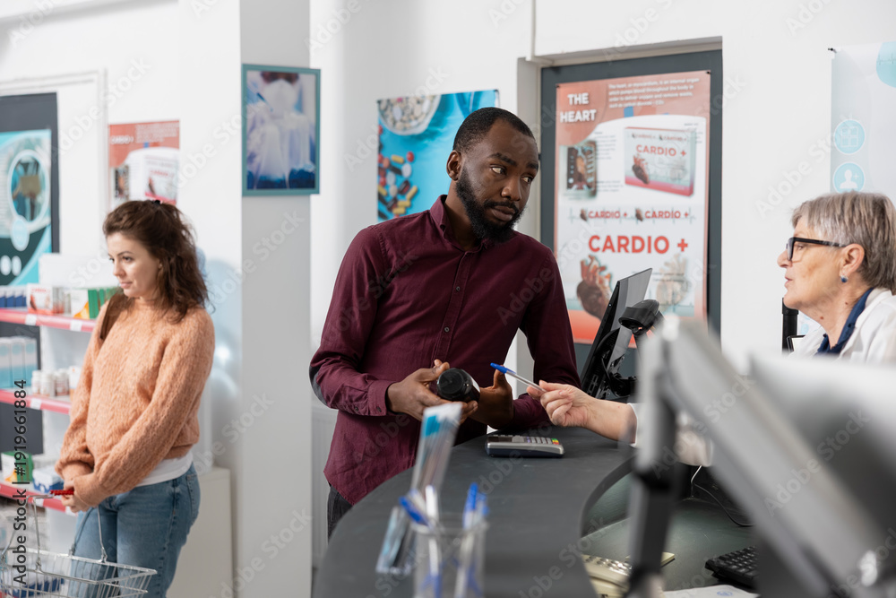 Obraz premium Senior female pharmacist provides medication information at pharmacy counter. Healthcare worker consults with black customer, explaining pill bottle and ensuring proper guidance in local dispensary.