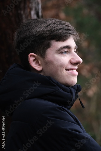 Male in black winter jacket. Smiling young guy. Side view, profile