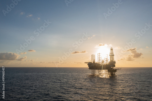 Aerial view from a drone of big jack up offshore drilling oil rig, production platform and supply vessel In the ocean during sunset - Oil and Gas Industry