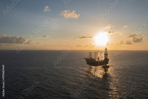 Aerial view from a drone of big jack up offshore drilling oil rig, production platform and supply vessel In the ocean during sunset - Oil and Gas Industry